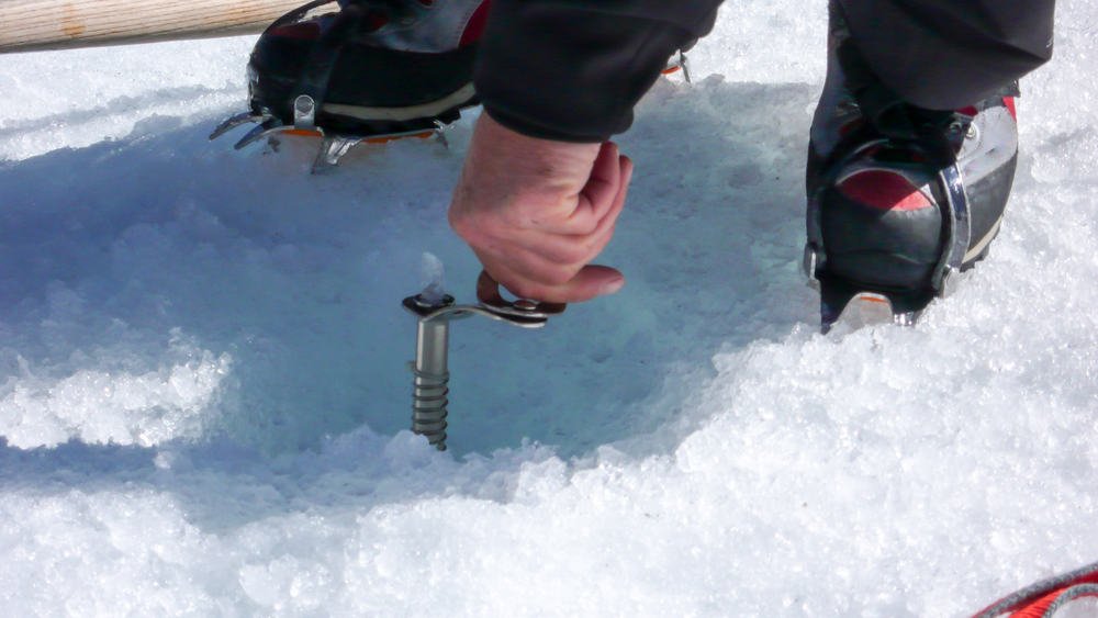 Mann befestigt Eisschraube im Eis